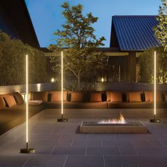 an outdoor fire pit surrounded by benches and trees at night time with lights on the sides