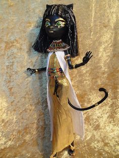 a statue of an egyptian woman with black hair and gold dress holding a cat's tail