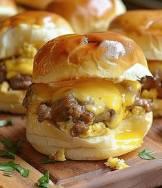 three cheeseburger sandwiches sitting on top of a wooden cutting board