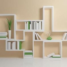 a white shelf filled with books next to a green vase and plant on top of it