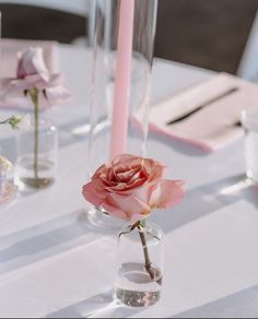 two pink roses in vases on a white table cloth with candles and napkins