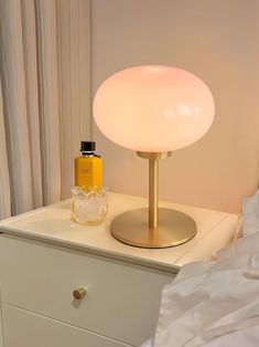 a table lamp sitting on top of a white dresser next to a bottle of perfume