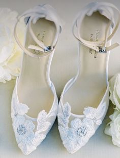 a pair of white shoes sitting on top of a table next to flowers