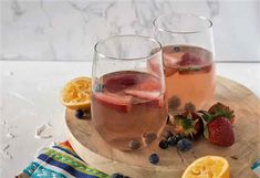 two glasses filled with liquid and fruit sitting on a wooden tray next to sliced lemons