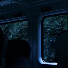 the inside of a train car with two windows and trees in the background at night