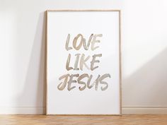 a white framed art print with the words love like jesus in gold foil on it