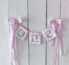 two pink ribbons with flowers on them hanging from the side of a white wooden wall