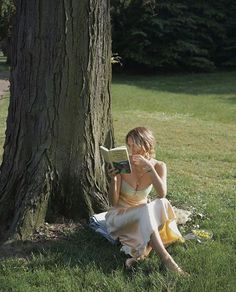 a woman sitting under a tree reading a book