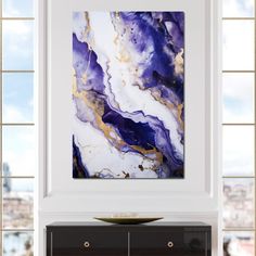 an abstract painting hangs on the wall above a black cabinet in a white and gold living room