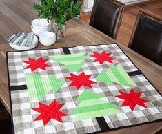 a quilted table runner with red and green stars on it, sitting on a dining room table