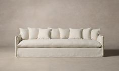 a white couch with six pillows on it's back and two sides, in front of a gray wall