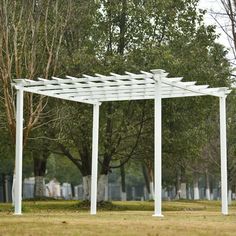 a white pergoline in the middle of a grassy area with trees behind it