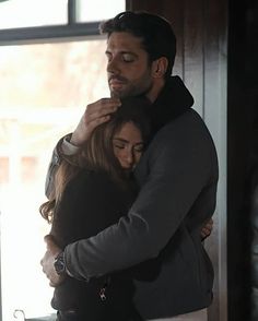 a man and woman embracing each other in front of a window