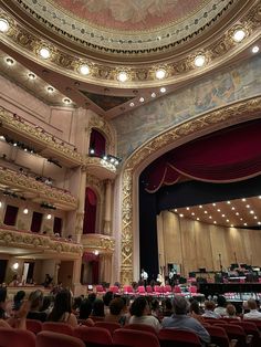 an auditorium filled with lots of people sitting in red chairs and looking up at the ceiling