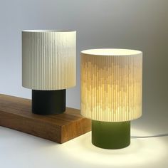 two lamps sitting next to each other on top of a wooden block in front of a white wall