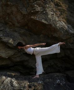 a woman is doing yoga on the rocks