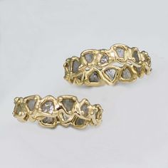 two yellow gold rings with white diamonds in them on a white surface, one is made out of metal and the other has an intricate design