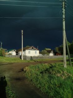 storm clouds loom in the sky over a small white house on a dirt road