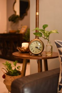 a clock sitting on top of a wooden table next to a vase filled with flowers