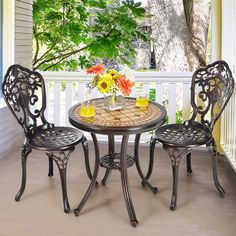 an outdoor table and chairs on a porch with flowers in the vase, next to a potted plant