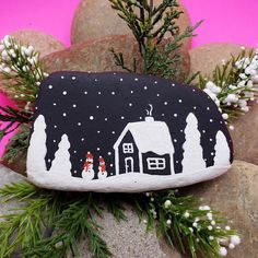 a painted rock with a house and snow scene on it, sitting next to some rocks