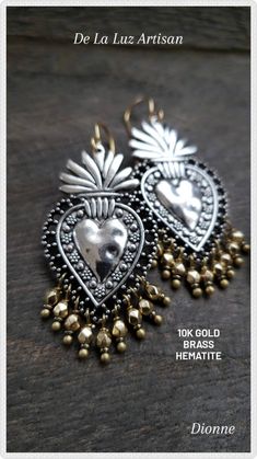 two silver heart shaped earrings with gold beads on a wooden surface and the words de la luz artisann written in spanish