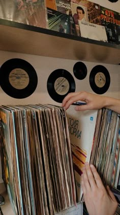 a record player is picking up records from the shelf in front of him and another person's hand reaching for them