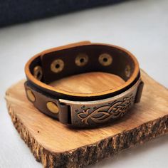 This handcrafted bracelet combines rugged leather with an intricate metal accent, creating a bold yet timeless look. The adjustable snap closure ensures a comfortable fit, while the engraved metal centerpiece adds a touch of unique detail. Perfect for those who appreciate rustic, durable accessories with a modern edge. Rustic Leather Strap Jewelry Gift, Rustic Adjustable Leather Strap Bracelets, Rustic Jewelry With Leather Strap For Gift, Rustic Leather Strap Bracelet Gift, Adjustable Rustic Jewelry With Leather Strap, Vintage Adjustable Leather Strap Wristband, Adjustable Engraved Leather Bracelet, Adjustable Brown Metal Cuff Bracelet, Vintage Leather Bracelet With Engraving