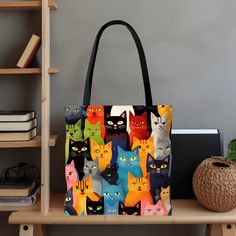 a multicolored tote bag with cats all over it on a wooden shelf