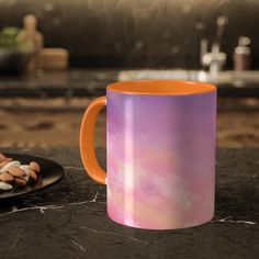 an orange and purple coffee mug sitting on top of a counter next to some cookies