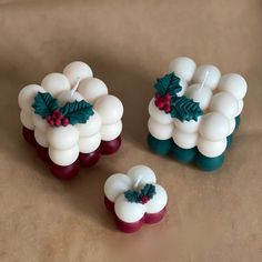 three candles with holly decorations on them sitting on a brown tablecloth covered surface in the shape of christmas wreaths