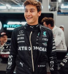 a man standing in front of a mercedes car at a race track with other people behind him