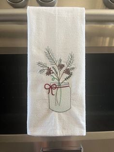 a kitchen towel hanging from the handle of an oven with flowers in a mason jar on it