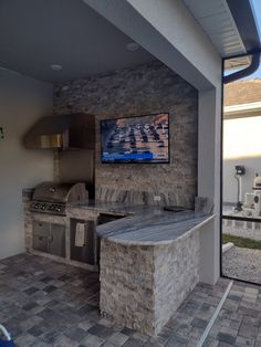 an outdoor kitchen with stone counter tops and stainless steel appliances on the outside wall, as well as a flat screen tv