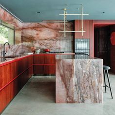 a large kitchen with marble counter tops and red cabinets, along with an island in the middle