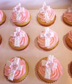 cupcakes decorated with pink frosting and white bows are arranged on a tray