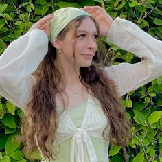 a woman with long hair wearing a white shirt and tie around her head standing in front of green leaves