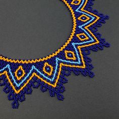 a blue and yellow beaded necklace on a gray surface with an oval shaped object in the middle