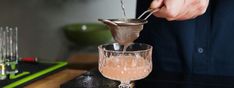 a person pours some liquid into a glass with a strainer in it on a table