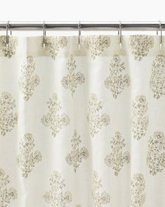 a white shower curtain with floral designs on it's side and metal rod ends