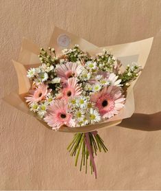 a bouquet of pink and white daisies is held by someone's hand against a beige wall