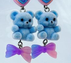 Add a touch of pastel goth cuteness to your outfit with these unique Blue Fuzzy Teddy Bear Kawaii Dangle Earrings! Featuring adorable heart beads and a sweet bow charm, these earrings are perfect for anyone who loves all things kawaii and cute. Stand out from the crowd with these one-of-a-kind accessories that are bound to make you smile every time you wear them. These handmade dangle earrings feature Cute AF fuzzy blue teddy bears adorned with pastel hearts and bows as sweet as candy. Get your thrillz on and add these one-of-kind earrings to your club wear collection. At Acid Thrillz, we value individuality and creativity by handmaking all items with care and saying F**k you to fast fashion by prioritizing quality and never creating duplicate items. Handmade Blue Kawaii Jewelry, Cute Handmade Light Blue Earrings, Cute Light Blue Earrings Gift, Cute Blue Earrings For Valentine's Day, Cute Light Blue Earrings For Gift, Blue Kawaii Earrings For Gift, Teddy Bear Kawaii, Bear Kawaii, Blue Teddy Bear