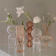 several vases with flowers in them sitting on a glass table top next to each other