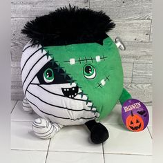 a green stuffed animal with black hair and fangs on it's face, sitting on a tile floor