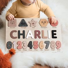 a baby holding up a wooden sign with numbers and shapes on it's face