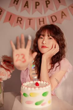 a woman sitting in front of a birthday cake with her hand up to the camera