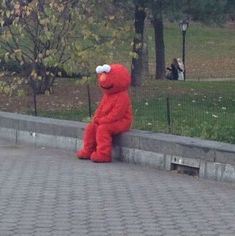 a large red stuffed animal sitting on the side of a road next to a park