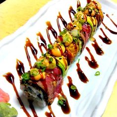 a sushi with sauce drizzled over it and garnished with vegetables