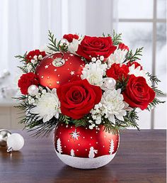 a vase filled with red and white flowers sitting on top of a wooden table next to a christmas ornament