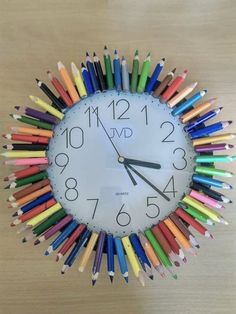 a clock made out of colored pencils on a wooden table with the time twelve o'clock